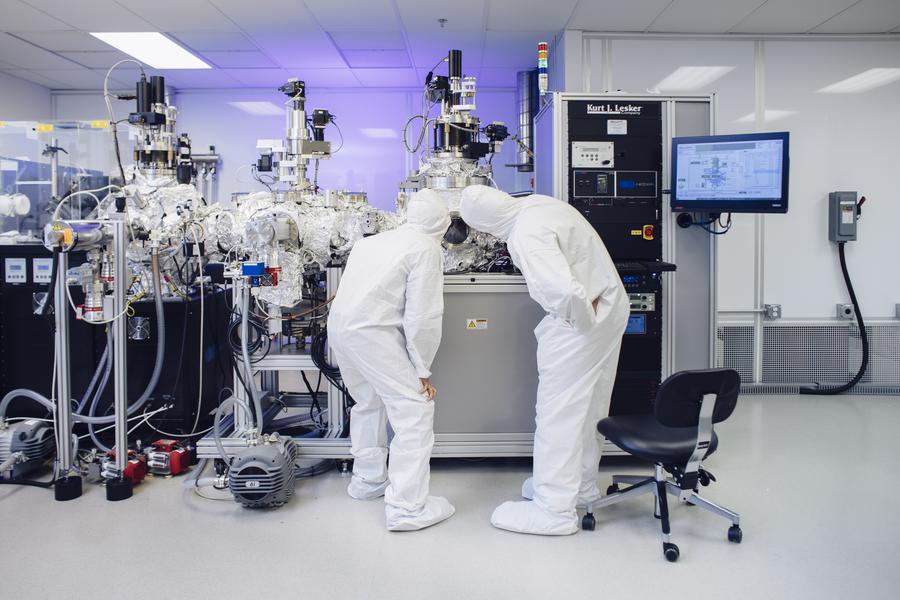 Two scientists in a clean room with white jumpsuits on observing and experiment.